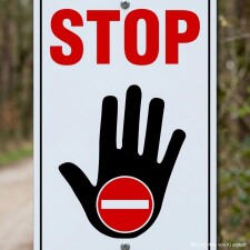 Das Bild zeigt ein Verkehrsschild mit dem Wort STOP in großen roten Buchstaben über einem schwarzen Handzeichen, das signalisiert, dass man anhalten soll. Dieses Schild wird häufig an Straßen oder Einfahrten verwendet, um Verkehrsteilnehmer auf eine Stoppsituation hinzuweisen.