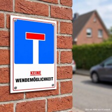Das Bild zeigt ein Verkehrsschild, das an einer Ziegelwand befestigt ist. Es hat einen blauen Hintergrund mit einem roten T-Symbol und der Aufschrift KEINE WENDEMÖGLICHKEIT in großen, roten Buchstaben, was darauf hinweist, dass es in dieser Straße keine Möglichkeit gibt, zu wenden.