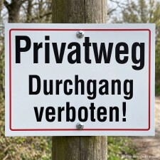 Das Bild zeigt ein Schild, das auf einem Holzpfosten angebracht ist und die Aufschrift Privatweg Durchgang verboten! trägt. Es ist deutlich sichtbar und warnt Passanten, dass der Weg privat ist und nicht betreten werden darf.