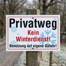 Das Bild zeigt ein Schild, das auf einem Holzpfosten befestigt ist und den Hinweis Privatweg sowie Kein Winterdienst! in großen, auffälligen Buchstaben enthält. Es warnt davor, den Weg in der Winterzeit auf eigene Gefahr zu benutzen, und ist in einem ländlichen Umfeld aufgestellt, wo der Weg von Bäumen umgeben ist.