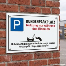 Das Bild zeigt ein Schild, das auf einem Ziegelmauerwerk angebracht ist. Es weist darauf hin, dass der Kundenparkplatz nur während des Einkaufs genutzt werden darf und warnt, dass unberechtigt abgestellte Fahrzeuge kostenpflichtig abgeschleppt werden.