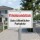 Das Bild zeigt ein Schild, das auf ein Privatgrundstück hinweist und darauf aufmerksam macht, dass es sich nicht um einen öffentlichen Parkplatz handelt. Das Schild ist weiß mit rotem und schwarzem Text und steht in einem Wohngebiet, um Autofahrer zu informieren, dass das Parken hier nicht erlaubt ist.