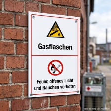 Das Bild zeigt ein Warnschild, das an einer Backsteinwand angebracht ist. Es weist darauf hin, dass in der Nähe von Gasflaschen Feuer, offenes Licht und Rauchen verboten sind, um Sicherheitsrisiken zu vermeiden.