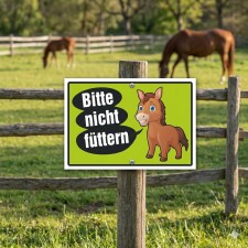 Das Bild zeigt ein Schild mit der Aufschrift „Bitte nicht füttern“ auf einem leuchtend grünen Hintergrund. Das Schild ist in einem Pferdegehege aufgestellt und enthält eine cartoonartige Darstellung eines Pferdes, um Passanten darauf hinzuweisen, dass das Füttern der Tiere nicht erlaubt ist.