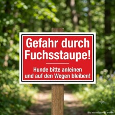 Das Bild zeigt ein rotes Warnschild mit der Aufschrift „Gefahr durch Fuchsstaupe!“. Es befindet sich in einem Waldgebiet und weist darauf hin, dass Hunde angeleint werden sollen und auf den Wegen bleiben müssen, um die Sicherheit zu gewährleisten.