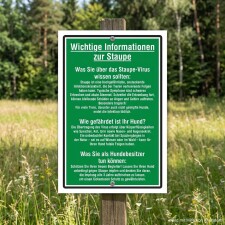 Das Bild zeigt ein informatives Schild im Freien, das wichtige Hinweise zur Staupe für Hundebesitzer enthält. Es beschreibt die Krankheit, ihre Symptome und die Gefahren für Hunde sowie präventive Maßnahmen, um die Tiere zu schützen.