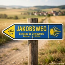 Das Bild zeigt ein Schild, das den Jakobsweg nach Santiago de Compostela anzeigt. Es ist blau mit gelben Akzenten und weist auf eine verbleibende Distanz von 2073 km hin, sowie auf ein Datum und den Namen Andreas.